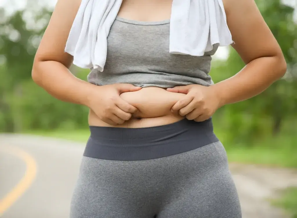 Woman measuring her waist with a tape measure, frustrated by stubborn belly fat despite diet and exercise