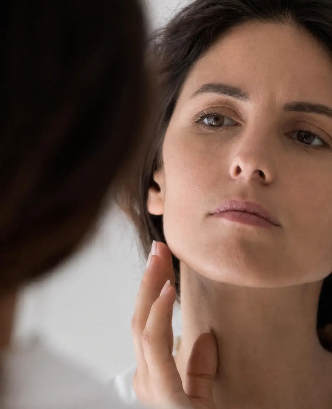Woman examining her lower face and jawline while considering treatment options for jowls and sagging skin